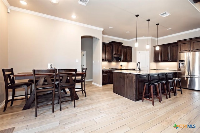 kitchen featuring visible vents, a kitchen island with sink, stainless steel appliances, dark brown cabinetry, and light wood-type flooring