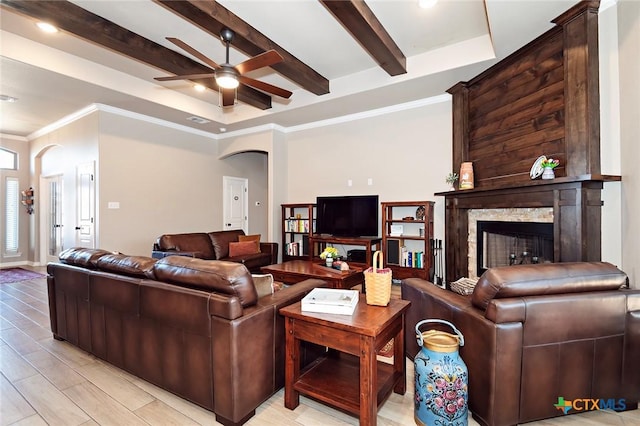 living area with crown molding, ceiling fan, beam ceiling, a fireplace, and arched walkways