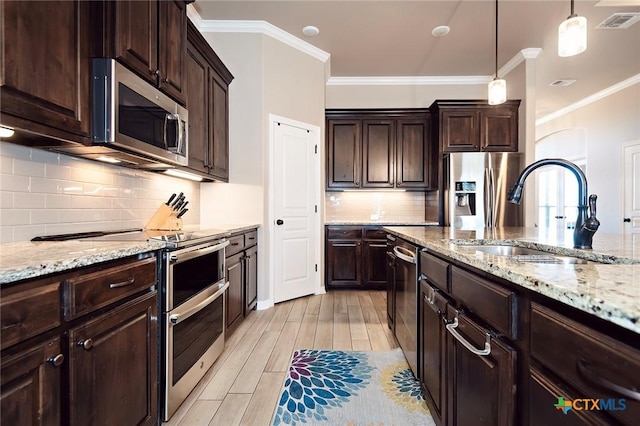 kitchen with visible vents, a sink, ornamental molding, stainless steel appliances, and decorative light fixtures