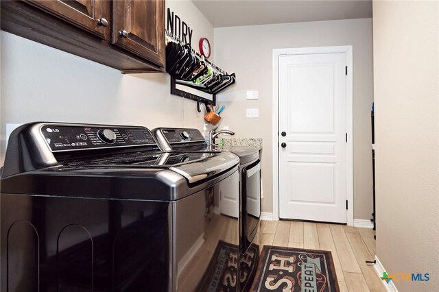 clothes washing area featuring baseboards, wood finish floors, washing machine and clothes dryer, cabinet space, and a sink