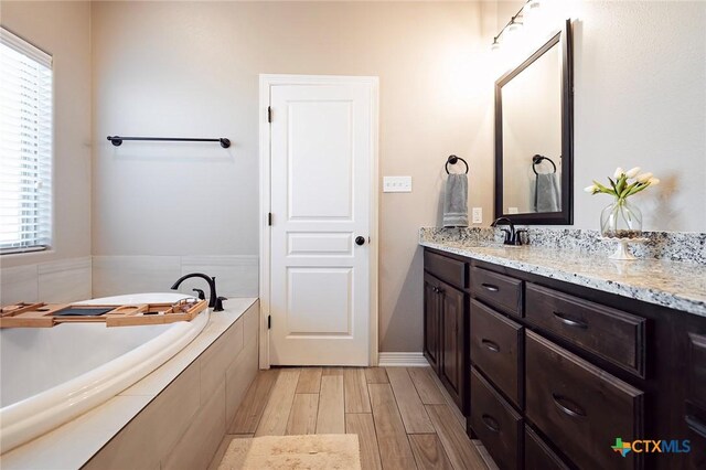 full bathroom featuring vanity, a garden tub, and wood finished floors