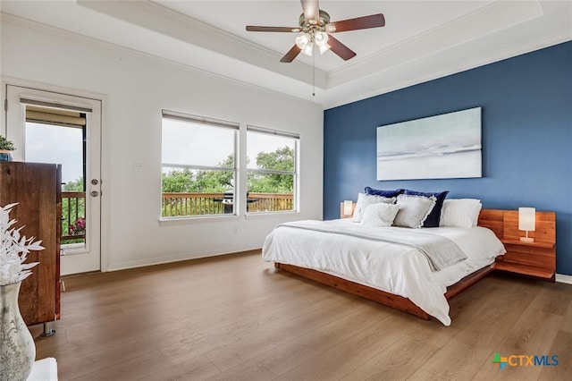 bedroom with a tray ceiling, access to exterior, crown molding, wood finished floors, and baseboards