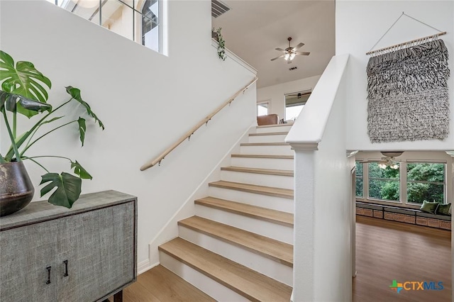 stairway with ceiling fan, a towering ceiling, and wood finished floors