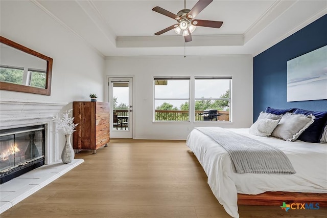 bedroom with wood finished floors, a raised ceiling, a glass covered fireplace, crown molding, and access to exterior