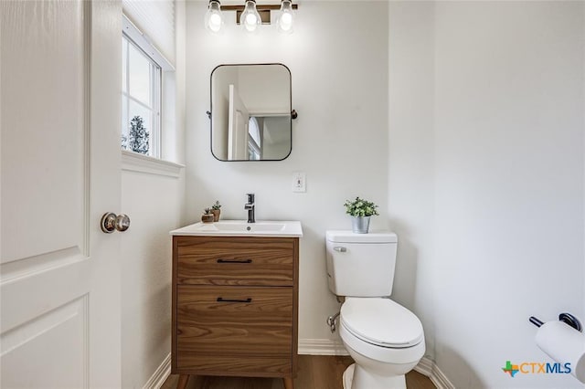 half bath featuring toilet, vanity, wood finished floors, and baseboards