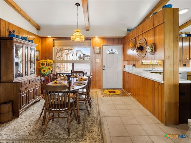 dining room featuring beamed ceiling, sink, light tile patterned floors, and wood walls