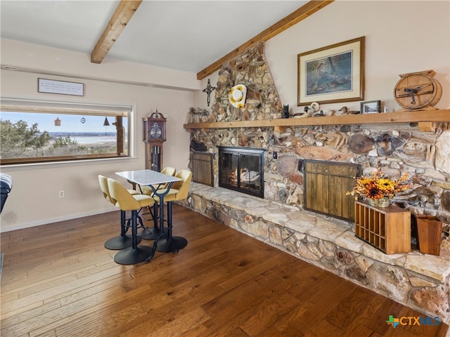 dining area with wood-type flooring, a stone fireplace, and vaulted ceiling with beams