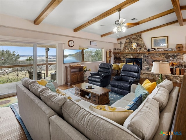 living room with hardwood / wood-style flooring, ceiling fan, a stone fireplace, and lofted ceiling with beams