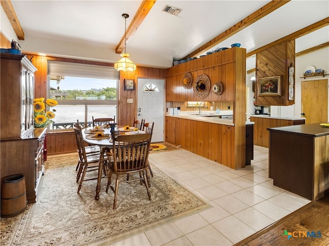 dining space featuring light tile patterned flooring, sink, lofted ceiling with beams, and wood walls