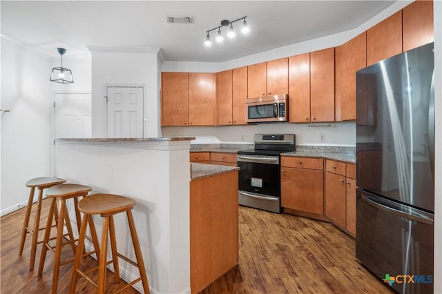 2502 Leon St Unit 201, Austin, TX 78705 - kitchen featuring brown cabinets, appliances with stainless steel finishes, a breakfast bar area, wood finished floors, and visible vents