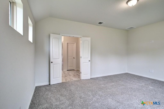 unfurnished room with carpet floors, baseboards, vaulted ceiling, and visible vents