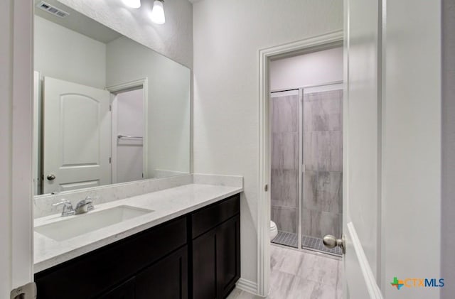 full bath with toilet, vanity, a shower stall, and visible vents