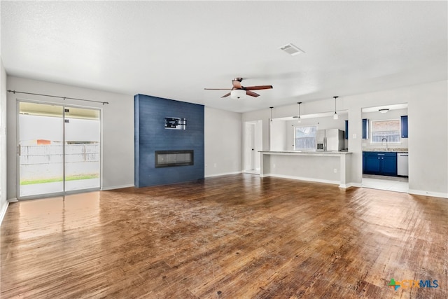 unfurnished living room featuring wood-type flooring, a large fireplace, ceiling fan, and sink