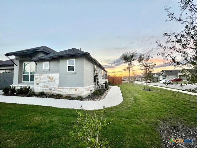 4201 Arques Ave, Round Rock, TX 78681 - property exterior at dusk with stone siding, a lawn, stucco siding, and a shingled roof