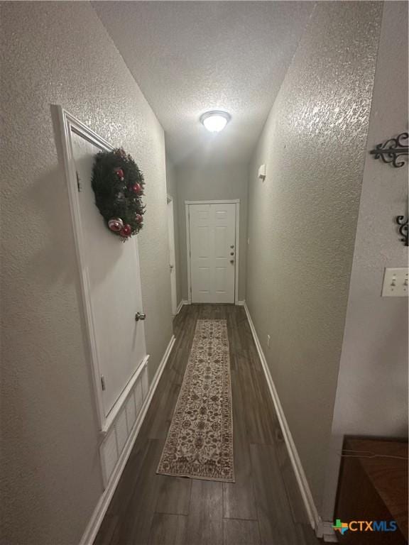 hallway featuring visible vents, baseboards, a textured wall, a textured ceiling, and dark wood-style flooring