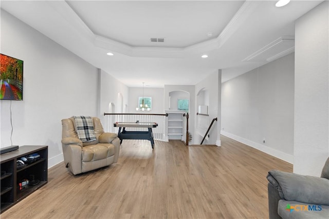 living area featuring ornamental molding, a raised ceiling, and light wood-type flooring