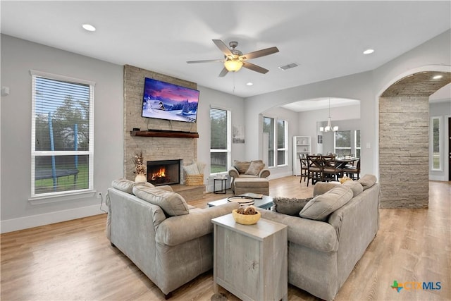 living room featuring a stone fireplace, ceiling fan with notable chandelier, and light wood-type flooring