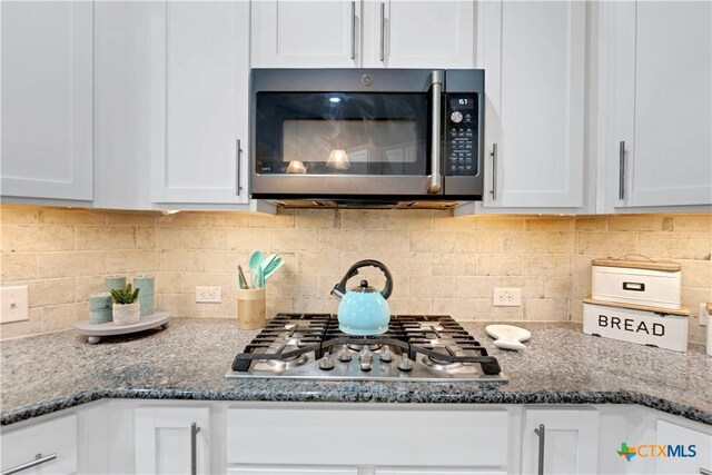 kitchen featuring white cabinetry, appliances with stainless steel finishes, tasteful backsplash, and dark stone counters