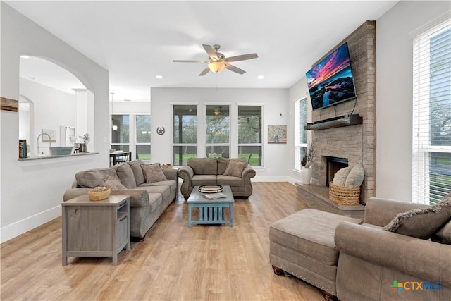 living room with ceiling fan, a fireplace, and light hardwood / wood-style floors