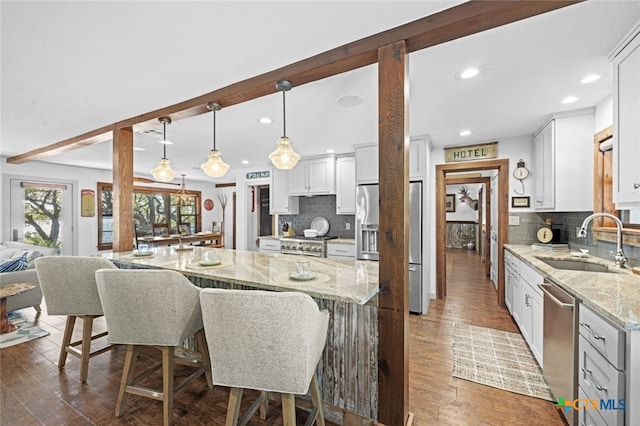 kitchen with beam ceiling, a breakfast bar area, stainless steel appliances, a sink, and light stone countertops