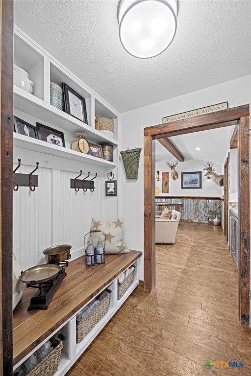 mudroom with built in shelves, a textured ceiling, and wood finished floors