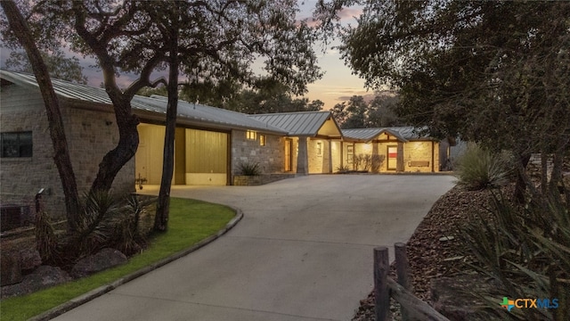 view of front facade with a standing seam roof, stone siding, metal roof, and concrete driveway