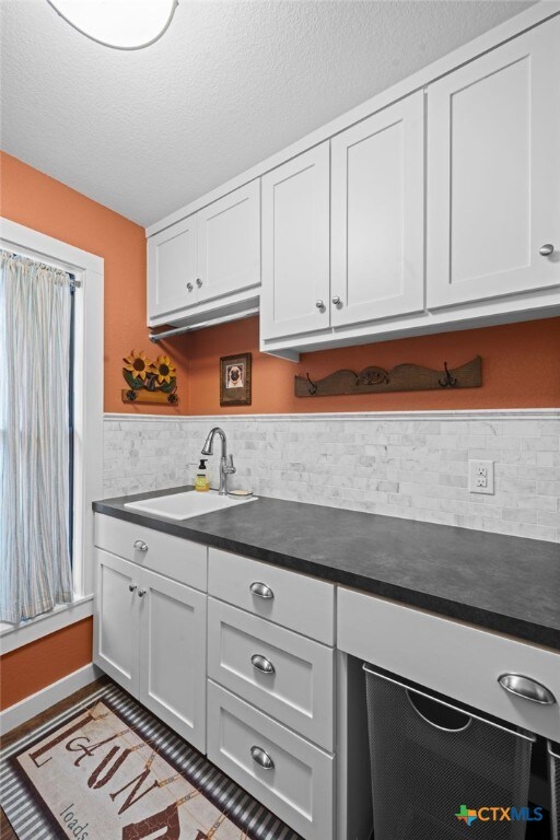 kitchen featuring dark countertops, white cabinets, a sink, and a textured ceiling