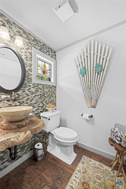 bathroom with toilet, wood finished floors, a sink, visible vents, and baseboards