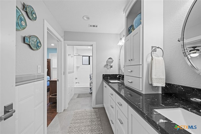 full bathroom featuring a textured ceiling, double vanity, a sink, and visible vents