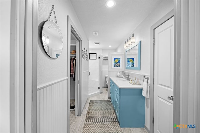 full bathroom featuring visible vents, a spacious closet, a stall shower, wainscoting, and vanity