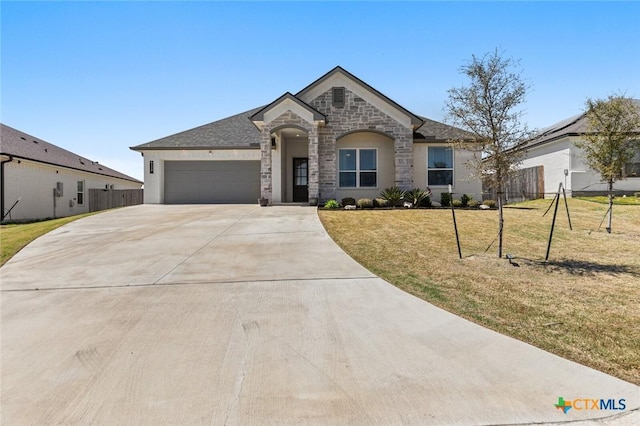 french country inspired facade with stone siding, a front yard, concrete driveway, and fence