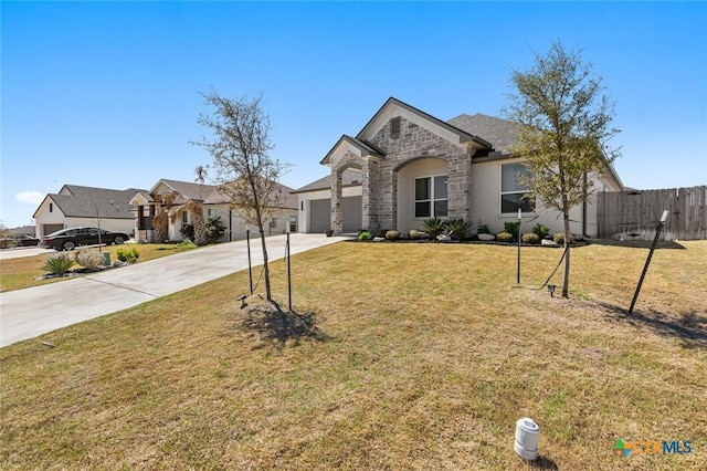 french country inspired facade featuring stone siding, concrete driveway, fence, a front lawn, and a garage