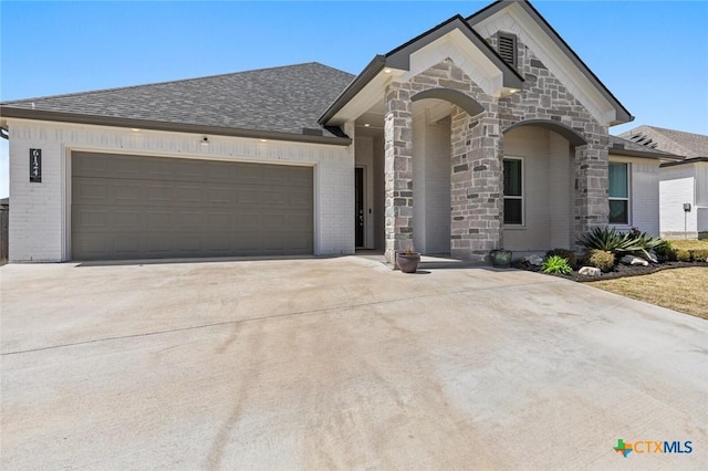 view of front facade with an attached garage, stone siding, driveway, brick siding, and a shingled roof