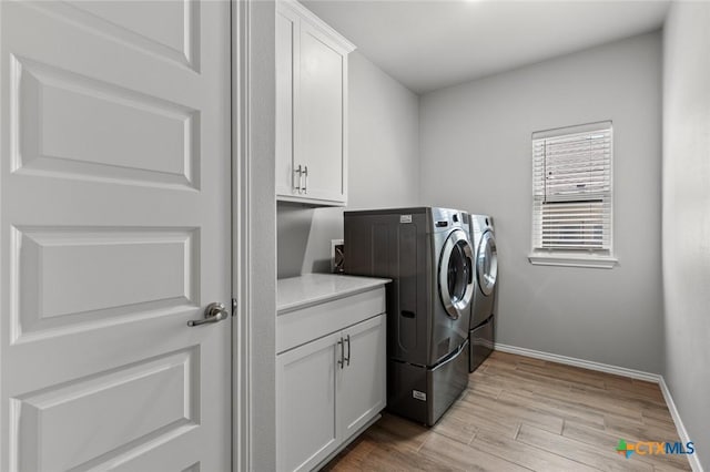 laundry room with washing machine and clothes dryer, cabinet space, baseboards, and light wood-style floors