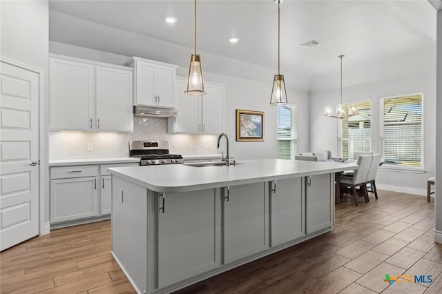 kitchen with a sink, tasteful backsplash, under cabinet range hood, gas range, and visible vents