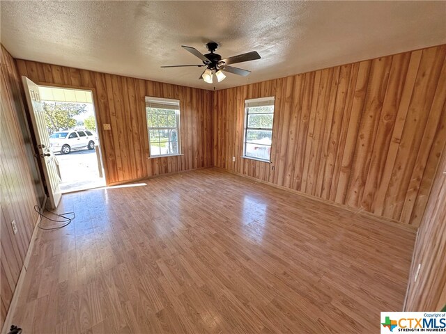 spare room with hardwood / wood-style floors, ceiling fan, wooden walls, and a textured ceiling