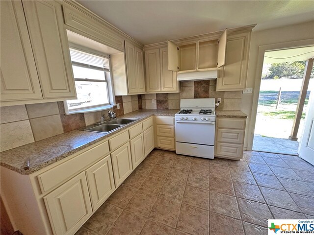 kitchen featuring cream cabinetry, sink, tasteful backsplash, and white gas range oven