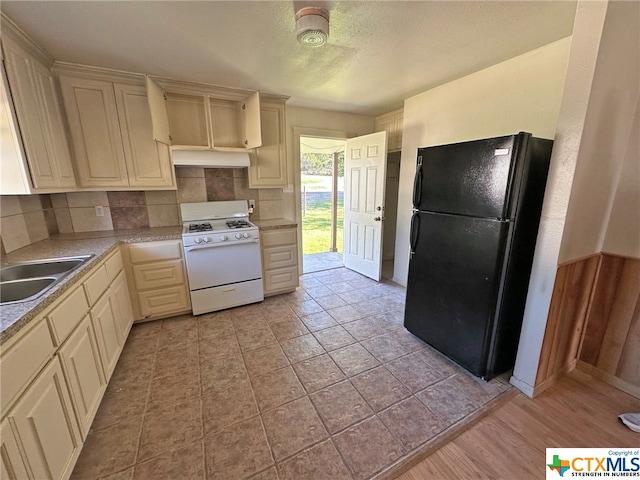 kitchen featuring black fridge, sink, tasteful backsplash, and white gas range oven