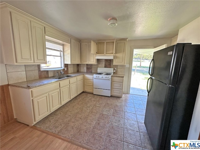 kitchen with black refrigerator, white range with gas stovetop, sink, and cream cabinets