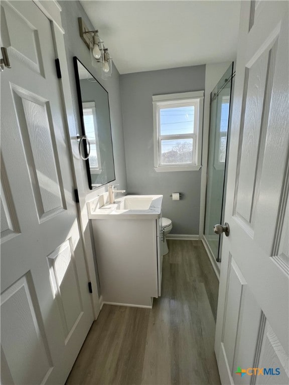 bathroom featuring vanity, wood-type flooring, a shower with shower door, and toilet