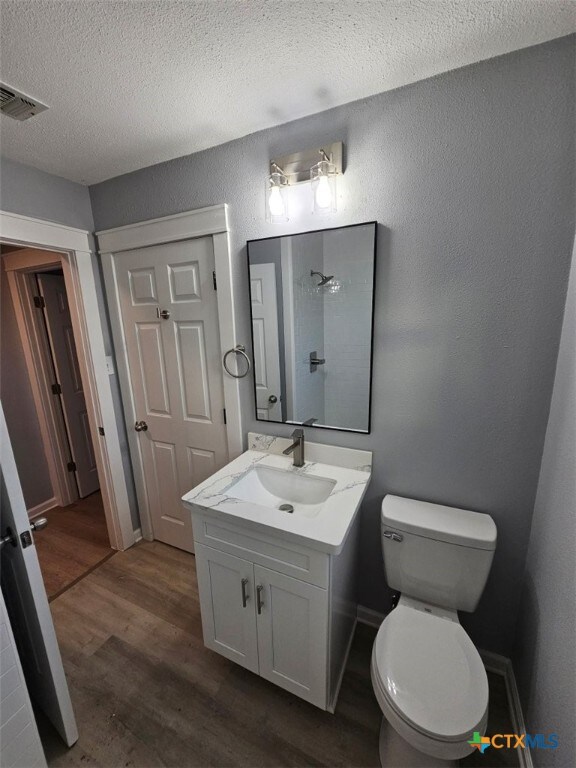 bathroom with hardwood / wood-style flooring, vanity, toilet, and a textured ceiling