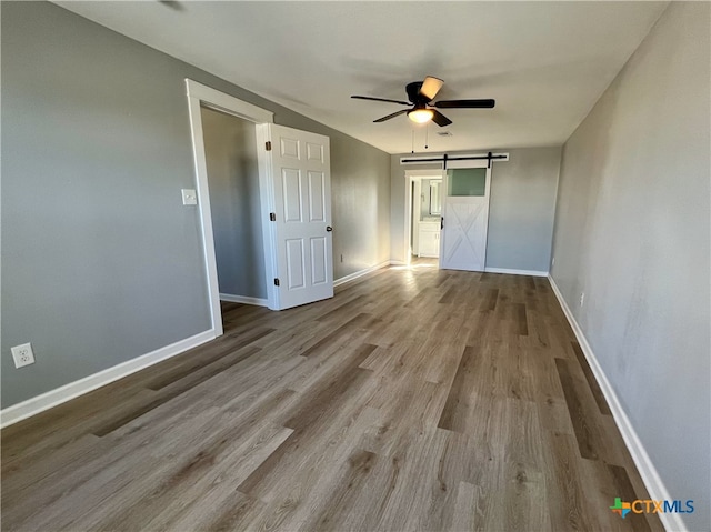 unfurnished bedroom with ceiling fan, a barn door, and light wood-type flooring