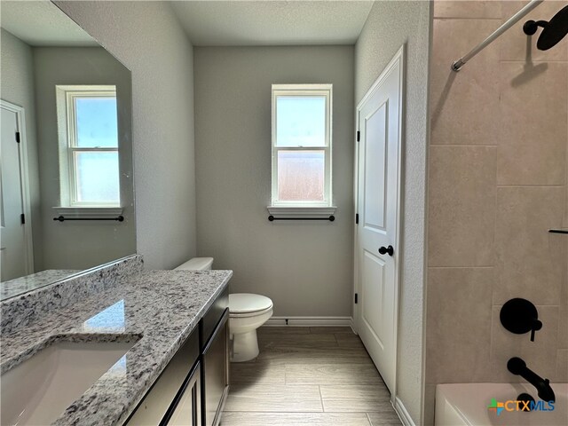 full bathroom featuring wood-type flooring, vanity, a textured ceiling, tiled shower / bath combo, and toilet