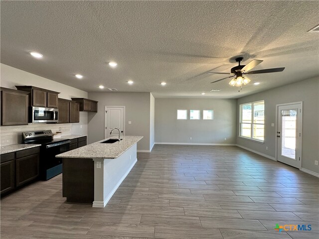 kitchen with sink, light stone counters, appliances with stainless steel finishes, a textured ceiling, and a kitchen island with sink