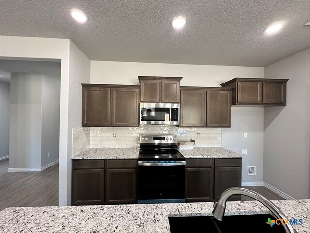 kitchen with stainless steel appliances, tasteful backsplash, light stone countertops, dark brown cabinets, and dark hardwood / wood-style flooring