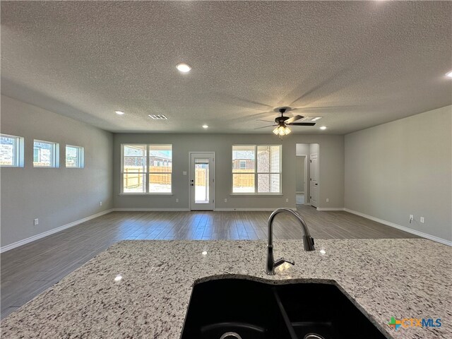 kitchen with sink, light stone countertops, ceiling fan, a textured ceiling, and wood-type flooring