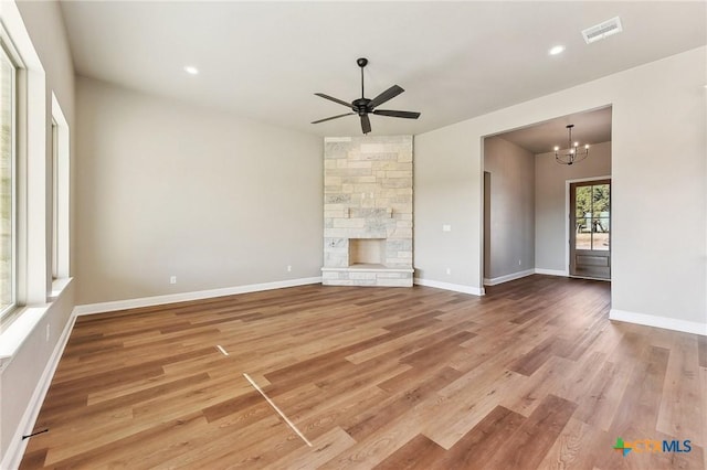 unfurnished living room with hardwood / wood-style floors, ceiling fan with notable chandelier, and a fireplace