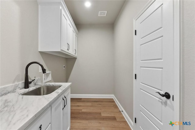 laundry room with cabinets, light hardwood / wood-style flooring, and sink