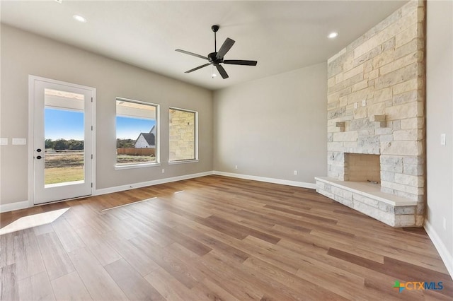 unfurnished living room with ceiling fan, light hardwood / wood-style floors, and a stone fireplace