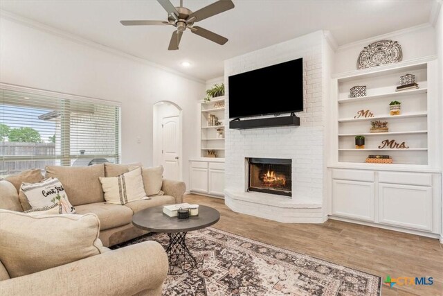 2619 Settlers Oak Dr, Belton, TX 76513 - living room featuring crown molding, light wood-type flooring, arched walkways, ceiling fan, and a brick fireplace